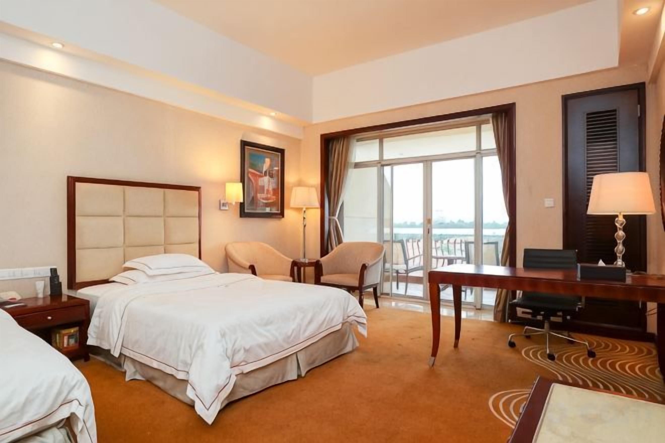 A hotel room with a bed, a desk, a chair, and a large window.