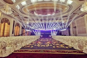 Ein prächtiger Saal mit einem langen, verzierten Teppich, Reihen weißer Stühle und einer Bühne mit blauem Hintergrund.