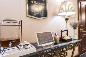 Una mesa de recepción con una cafetera, un cartel con números de contacto, una lámpara y un letrero de bienvenida.