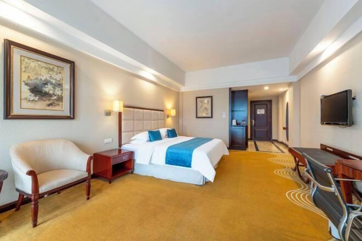Quarto de hotel com cama, uma cadeira, escrivaninha e televisão.