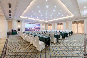 Un salón de conferencias con una larga mesa, sillas blancas y suelo alfombrado.