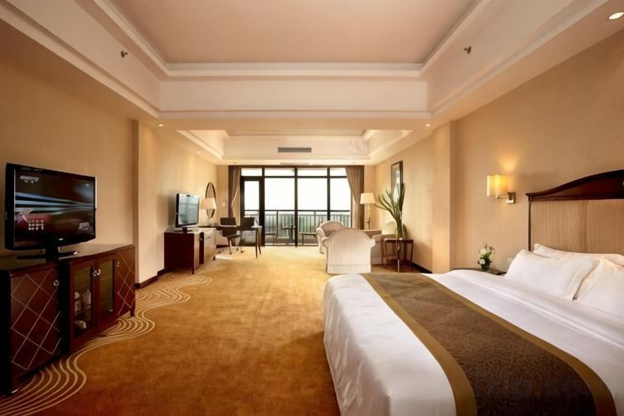 Ein Hotelzimmer mit einem großen Bett, einem Fernseher, einem Schreibtisch mit Stuhl und Blick ins Freie durch große Fenster.