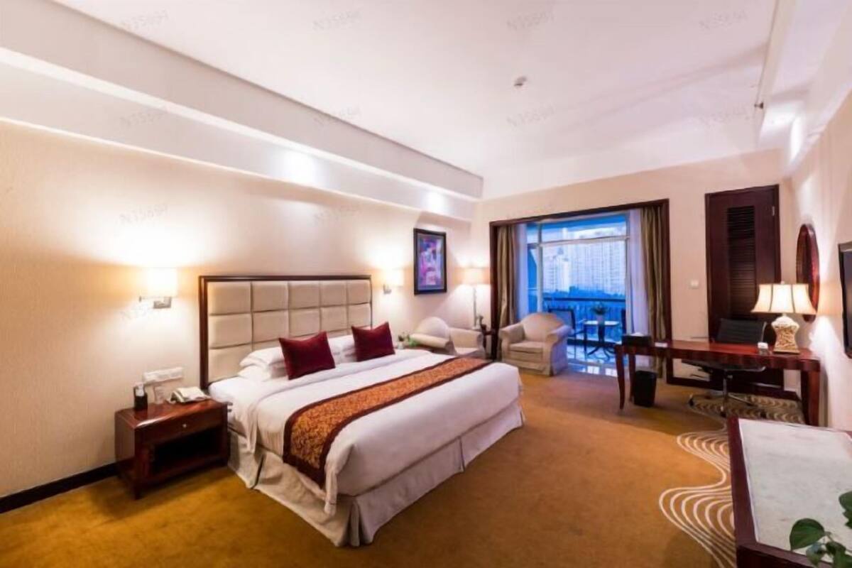Quarto de hotel com uma cama grande, uma escrivaninha, uma cadeira, uma mesinha e vista para uma varanda.