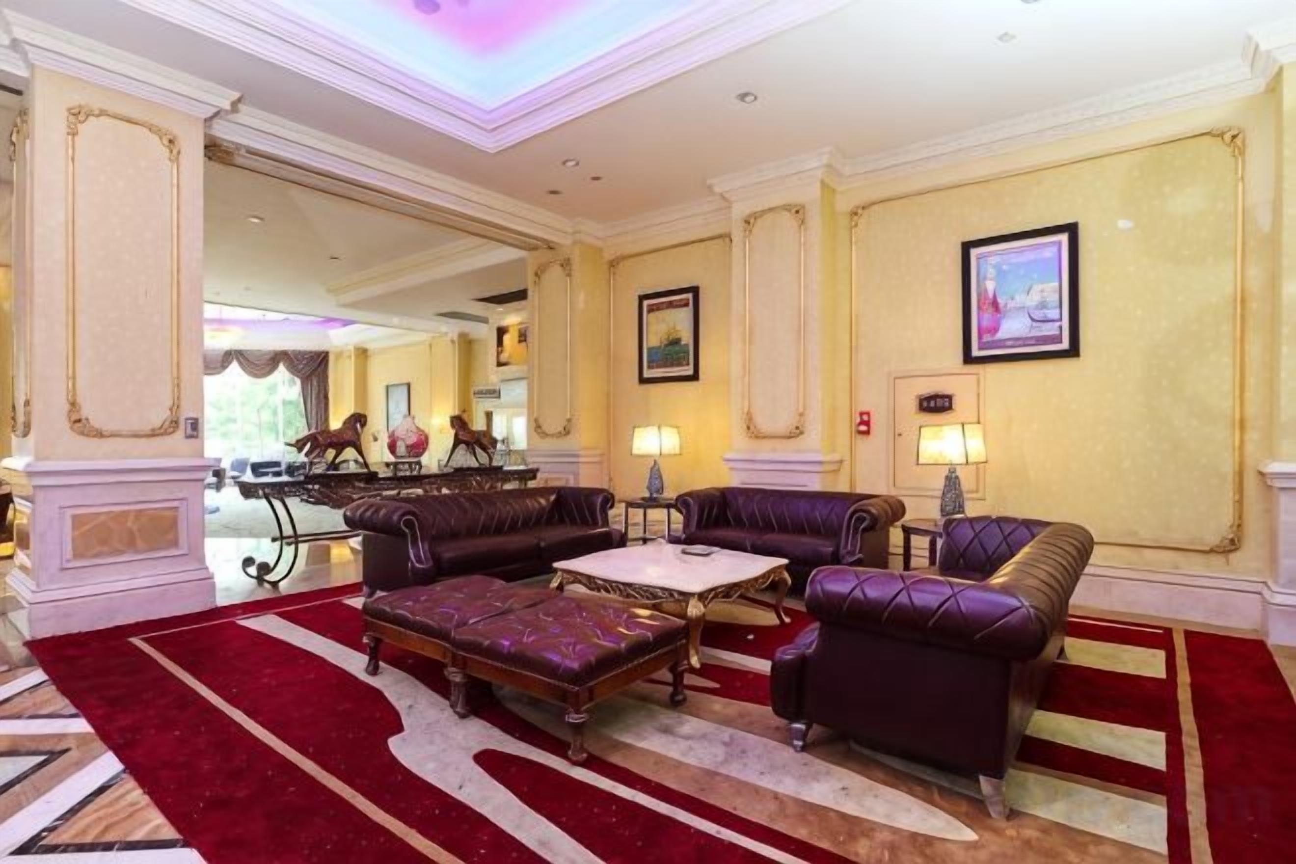 Un hall de hotel con alfombra roja, sofás de cuero, una mesa de centro y un candelabro.