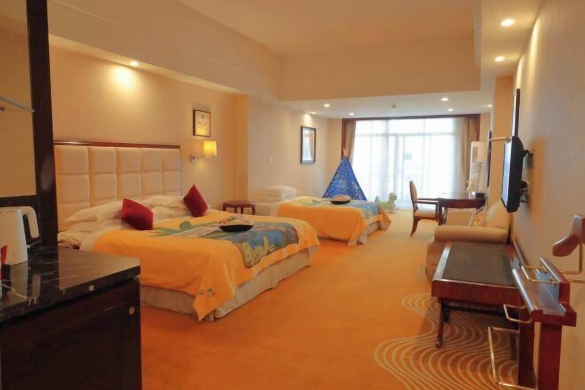 Quarto de hotel com duas camas, uma mesa, uma cadeira, televisão e uma janela com cortinas.