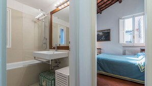A bathroom with a bathtub, a sink, and a mirror with lights. There is a window with a view of a building outside. - Three bedrooms in world-famous Via Giulia - Wifi, A/C, Washing machine (Roma)