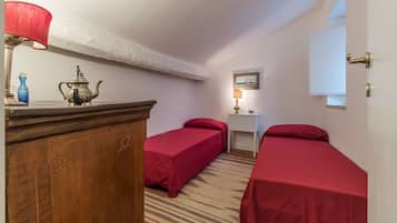 A small room with two single beds, a wooden dresser, a lamp, a small table with a lamp, and a framed picture on the wall.