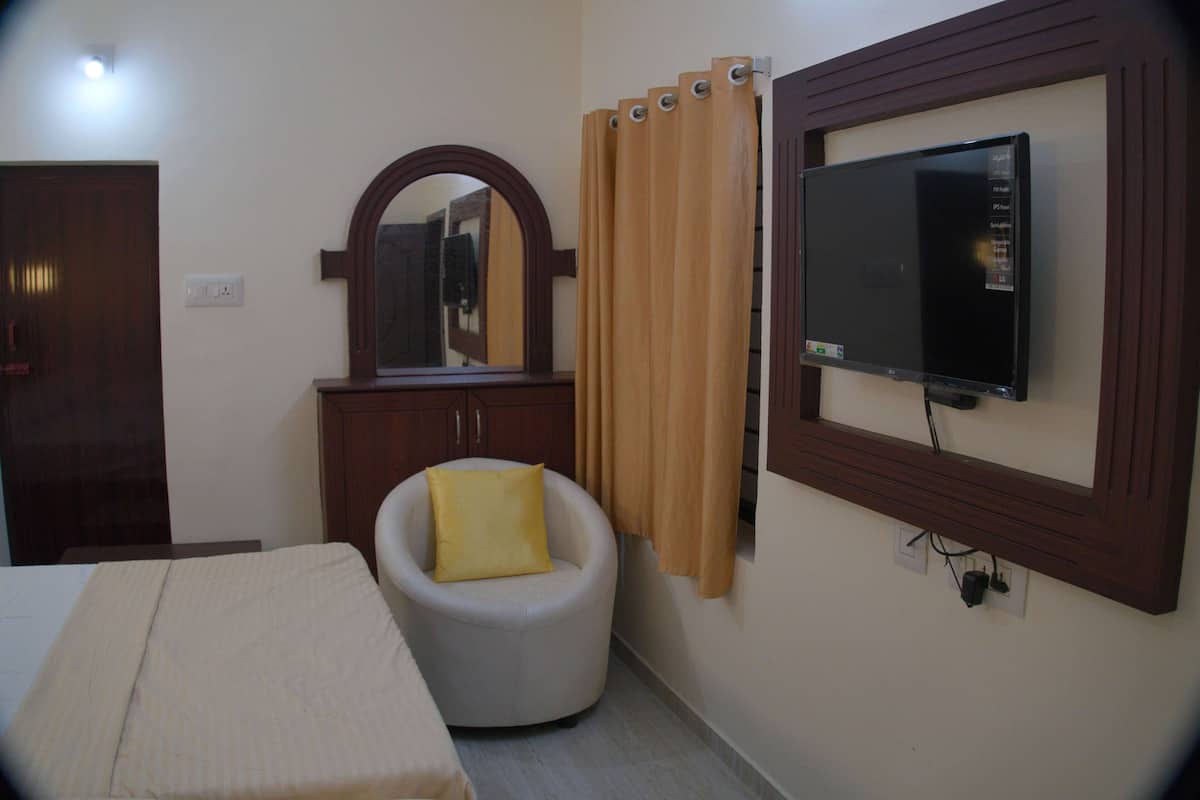 A hotel room with a bed, a chair, a TV mounted on the wall, a mirror, and a curtain.