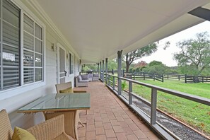 A covered patio with wicker furniture and a glass table, overlooking a fenced yard with trees. - Malolo Park Guest House in the Watagans - serenity (Quorrobolong)