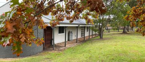 A house with a covered porch, a fenced yard, and a tree with autumn leaves.