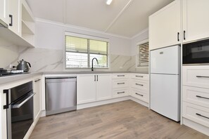 Una cocina moderna con armarios blancos, lavavajillas de acero inoxidable, horno empotrado y refrigerador.