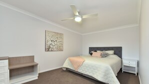 Un dormitorio con cama, mesita de noche, cómoda, ventilador de techo y una obra de arte en la pared.