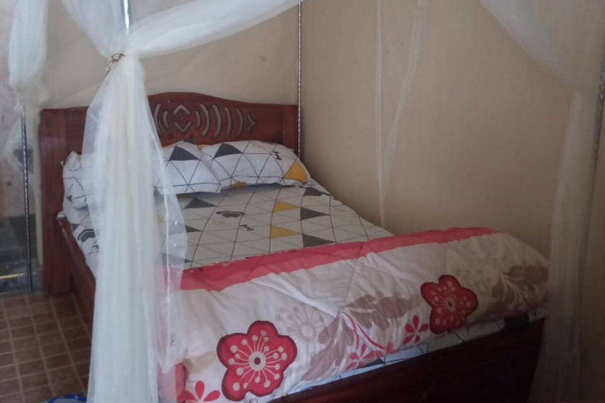 A single bed with a mosquito net, a wooden headboard, and a floral-patterned bedspread.