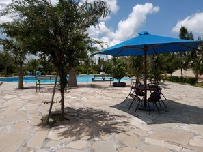 A poolside area with stone flooring, a blue umbrella, and a seating arrangement. - Wonderland Resort (Machakos)