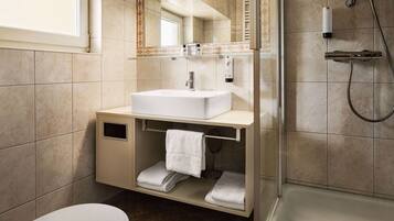 Un baño moderno con un lavabo blanco, una ducha con mampara de vidrio y un espejo sobre el lavabo.
