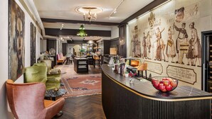 A modern hotel lobby with a curved reception desk, comfortable seating, and a large mural depicting historical scenes. - DORMERO PaHo Wels (Wels)