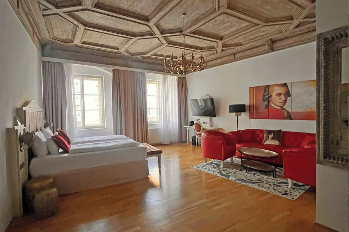 Una habitación con cama, sofá rojo, televisor y un cuadro en la pared.