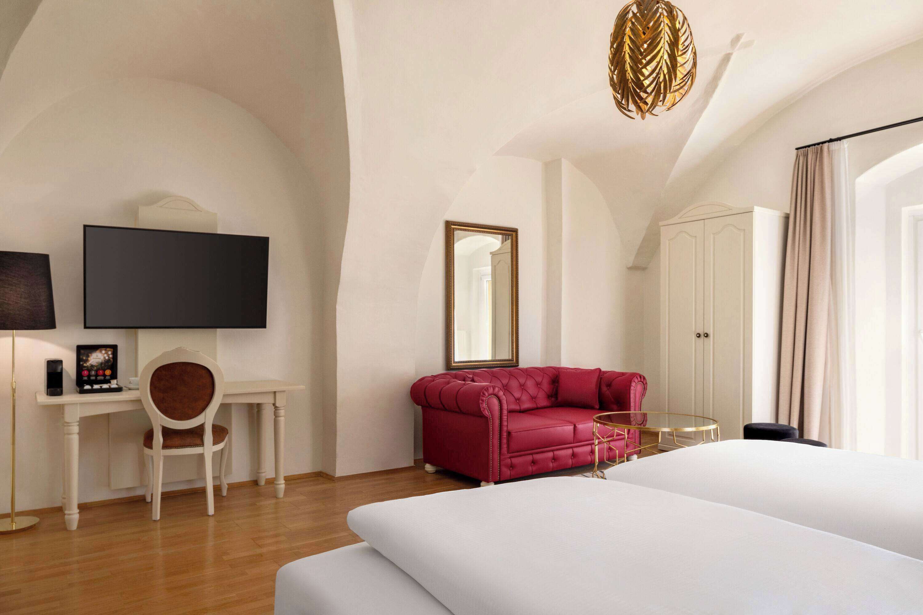Una habitación de hotel moderna con una cama grande, un sofá rojo, un escritorio con una silla, un televisor y un armario.