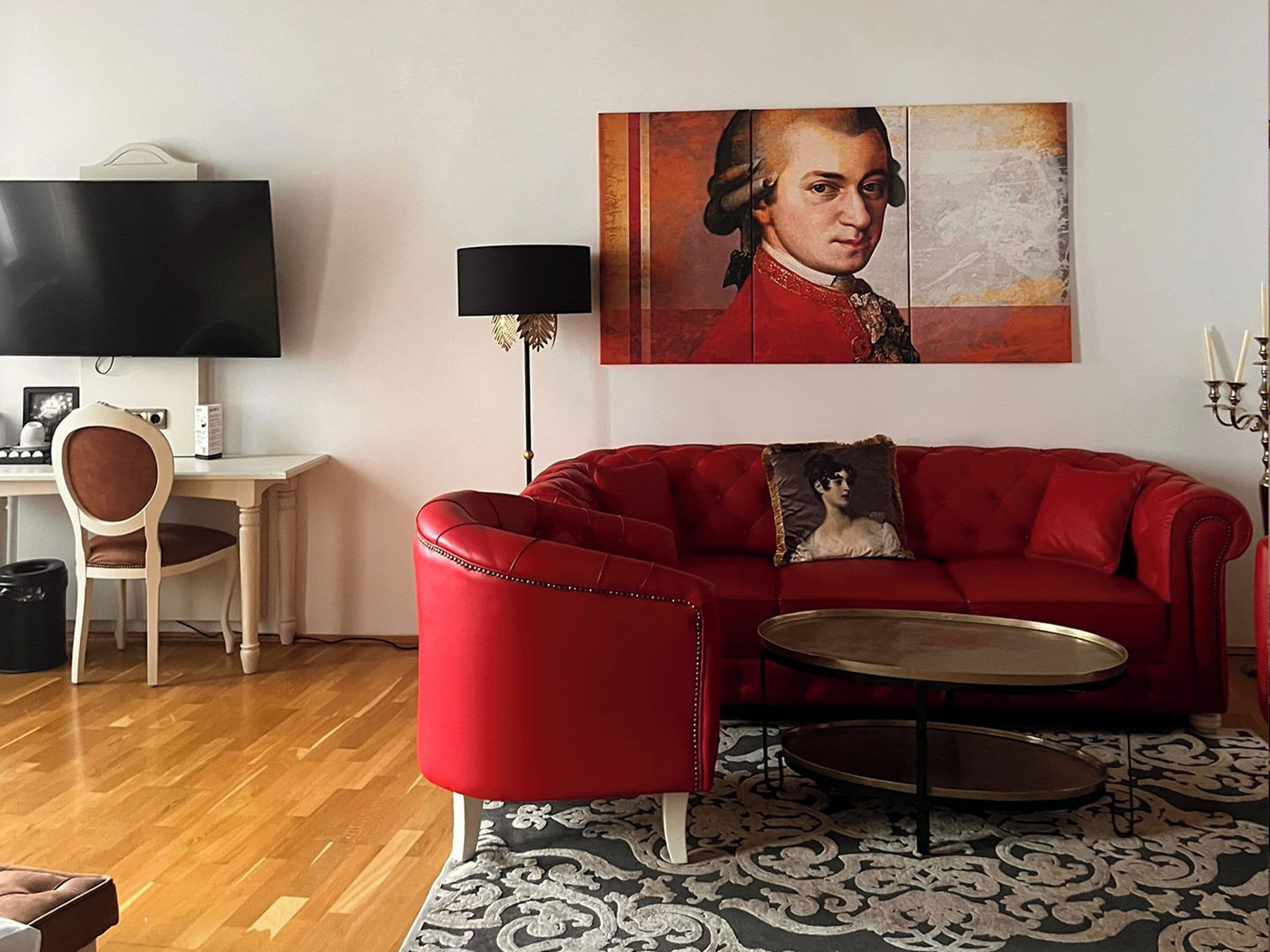 A living room with a red sofa, a small round table, a television, a lamp, and a portrait on the wall.