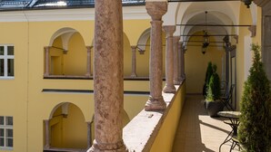 A yellow building with arched windows and columns, a tiled floor, and outdoor seating with potted plants. - DORMERO PaHo Wels (Wels)