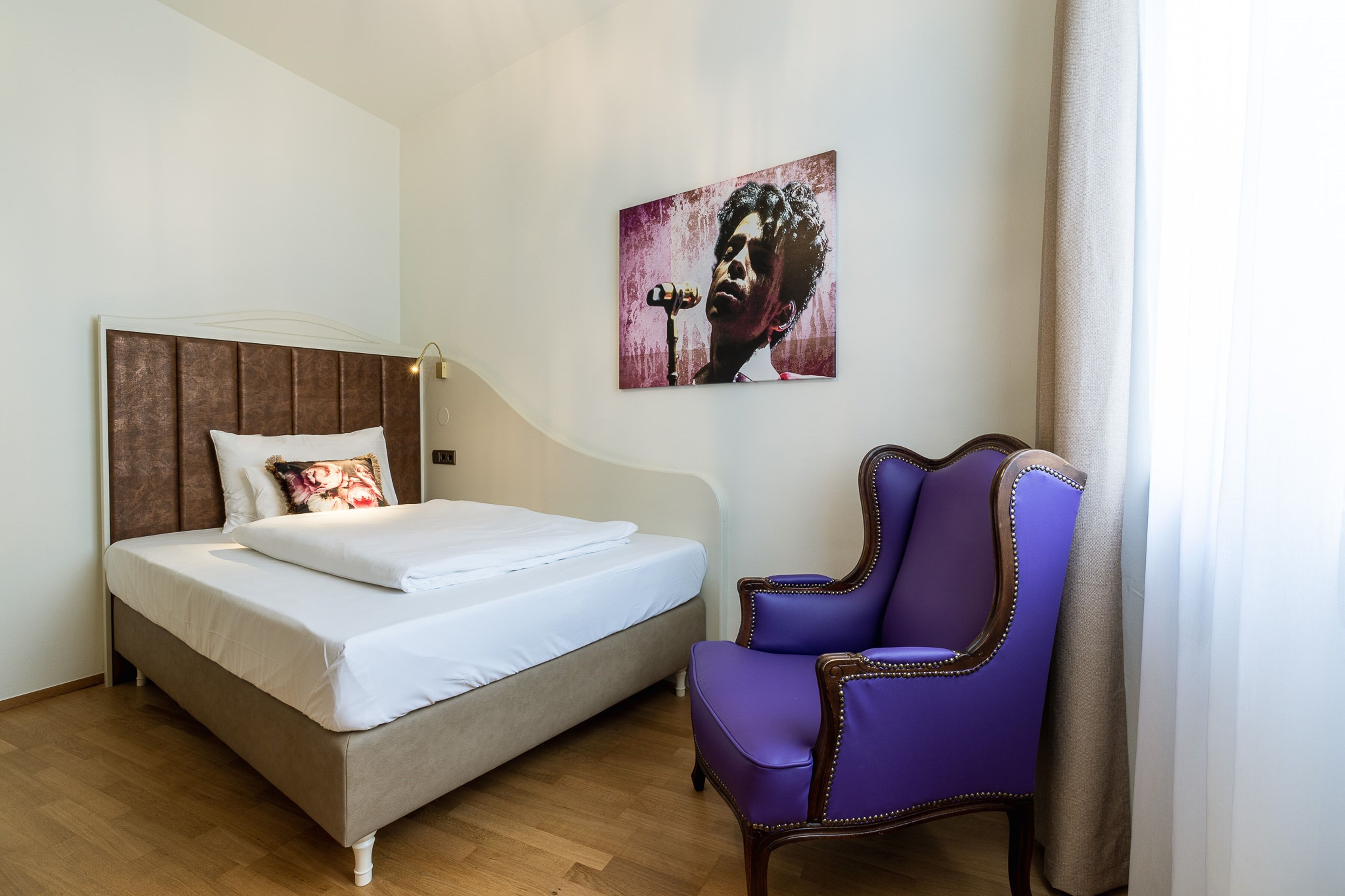 Ein Schlafzimmer mit einem Bett, einem violetten Sessel und einem Bild an der Wand.