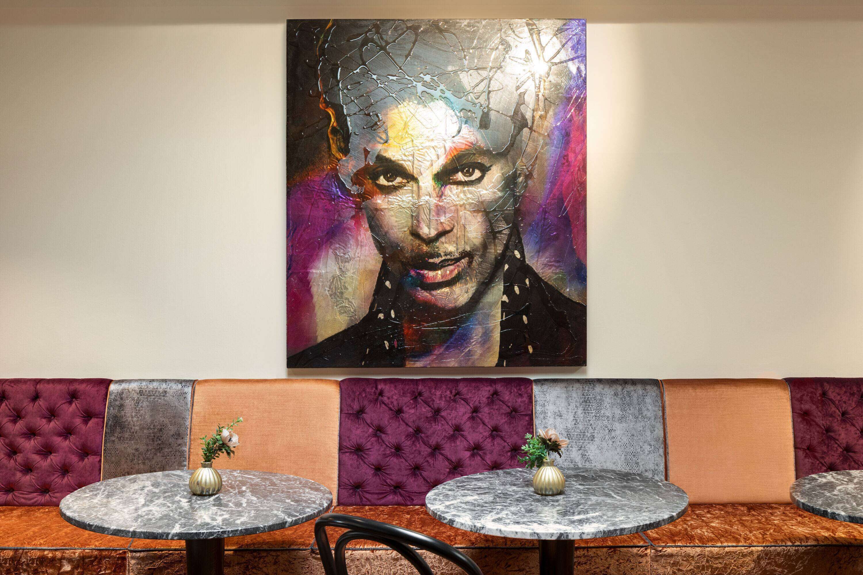 Een restaurant met een groot abstract schilderij aan de muur, zachte zitplaatsen en marmeren tafels.