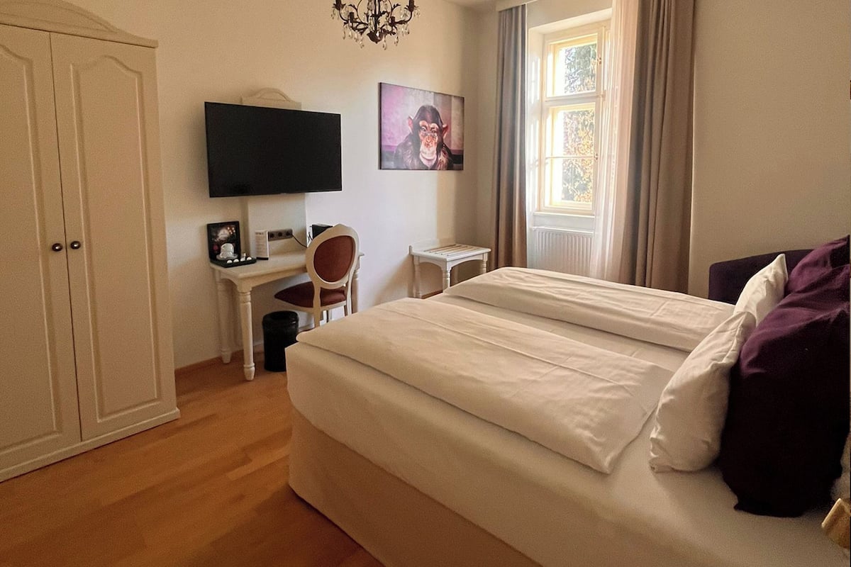 Un dormitorio con cama, escritorio, silla, televisor y ventana.
