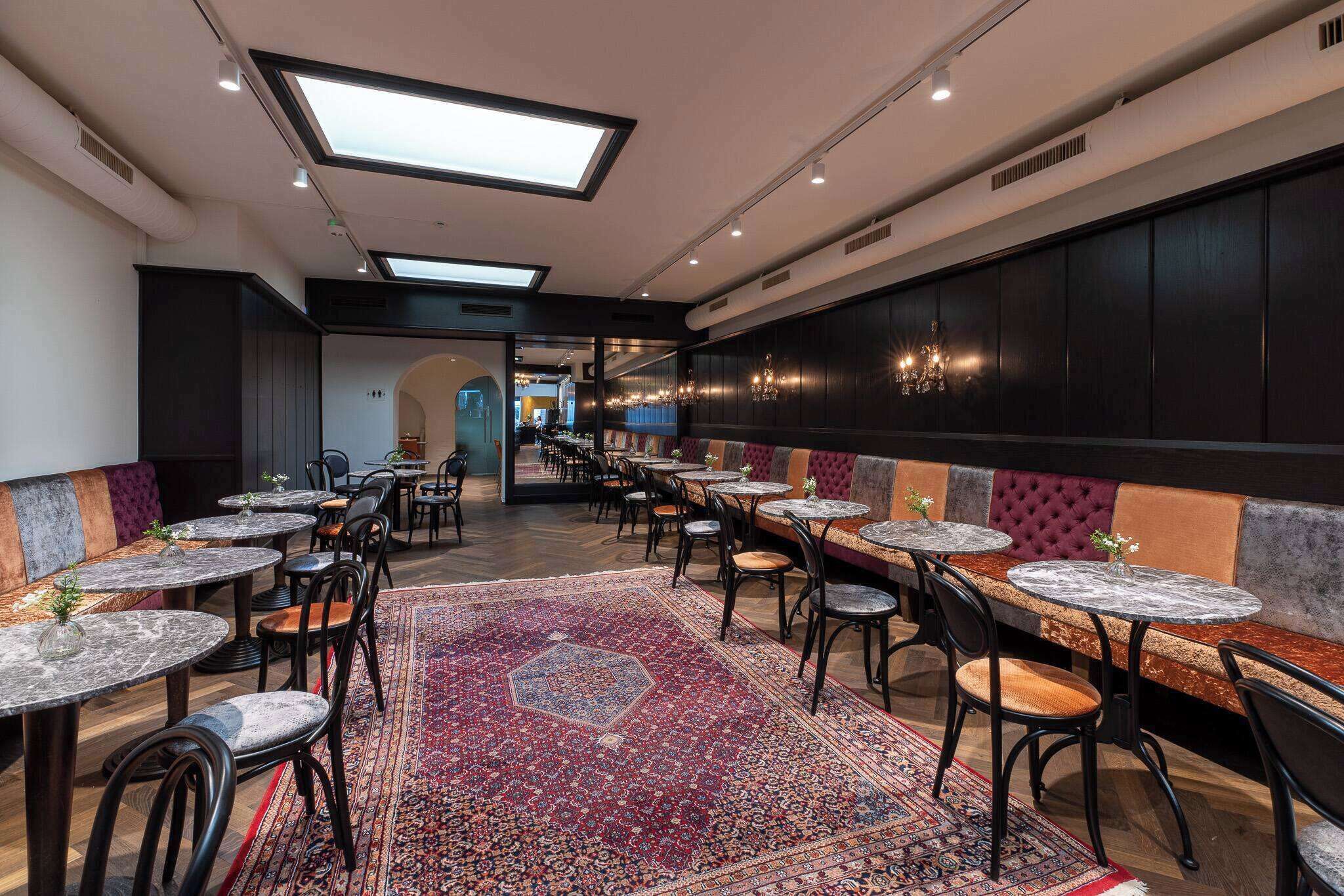 Um restaurante amplo com pé-direito alto, claraboias e diversas opções de assentos, incluindo mesas e cabines.