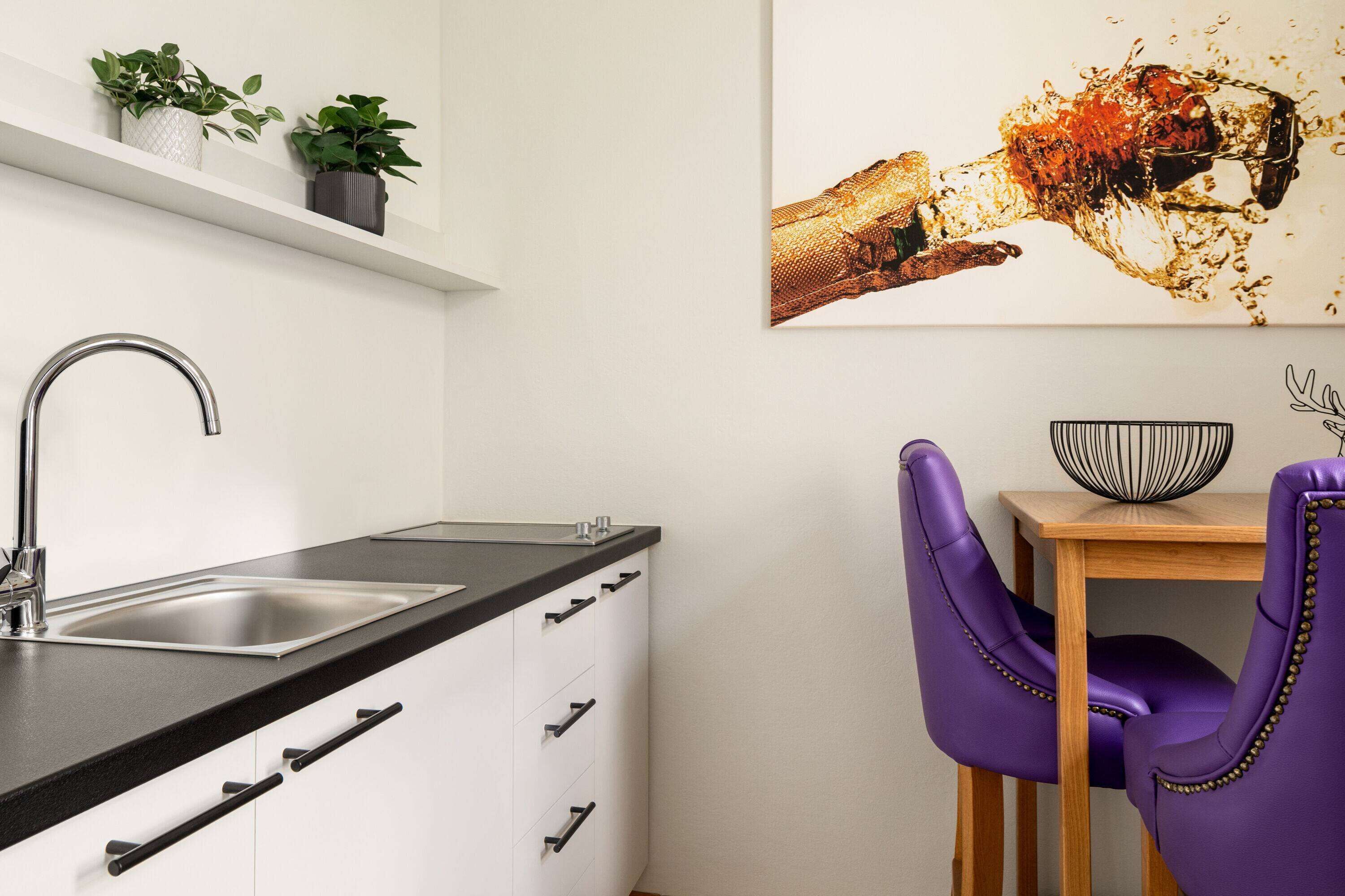 Una cocina moderna con un lavamanos de acero inoxidable, armarios blancos y una mesa de madera con una silla morada.