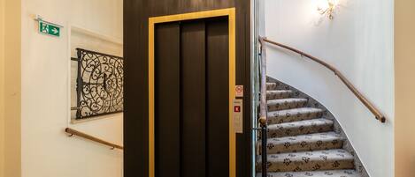 Una escalera con alfombra estampada y barandilla de madera, que lleva a una puerta oscura con marco dorado.