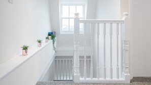 A white staircase with a balustrade, a small window, and potted plants on the landing. - Stunning 2 Bedroom Duplex Apt in Center of Camden (London)