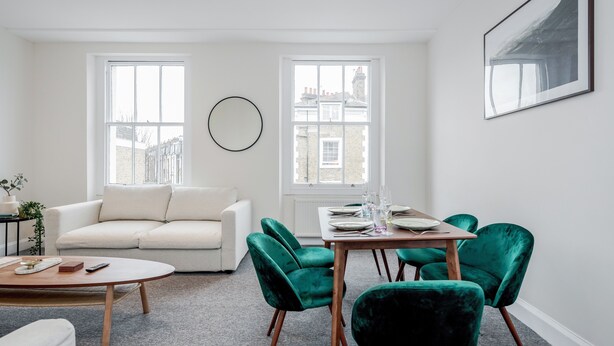 A modern living room with a sofa, a round coffee table, and a dining area with a table and chairs. - Stunning 2 Bedroom Duplex Apt in Center of Camden (London)