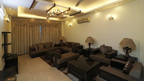 A modern living room with a sectional sofa, coffee table, and lamps. - Amar Villa One (New Delhi)