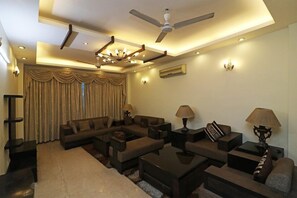 A modern living room with a sectional sofa, coffee table, and lamps. - Amar Villa One (New Delhi)