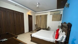 A hotel room with a bed, a desk, a chair, and a wardrobe. - Amar Villa One (New Delhi)