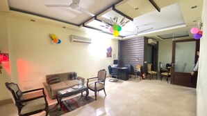 A spacious living room with a high ceiling, ceiling fans, a sofa set, a coffee table, and a dining area. - Amar Villa One (New Delhi)