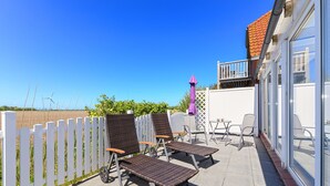 Un patio con mobiliario exterior, una cerca blanca y un edificio con balcón.