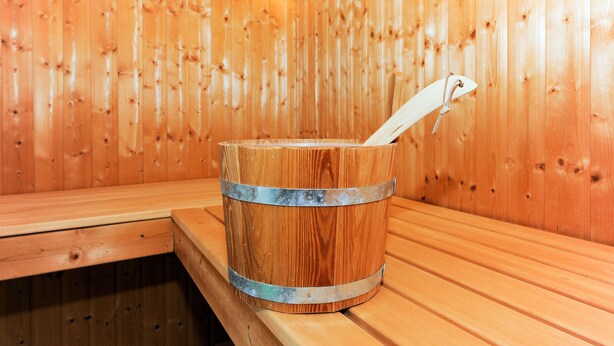 Una sauna de madera con un balde de metal y un banco.