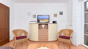 Una sala de estar con televisor, dos sillones de mimbre, una mesa de madera y un radiador blanco.