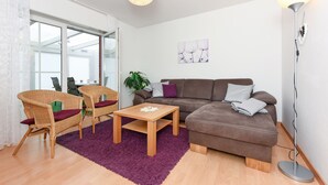 Una sala de estar moderna con un sofá marrón, dos sillas de mimbre, una mesa de centro de madera y un tapete morado.