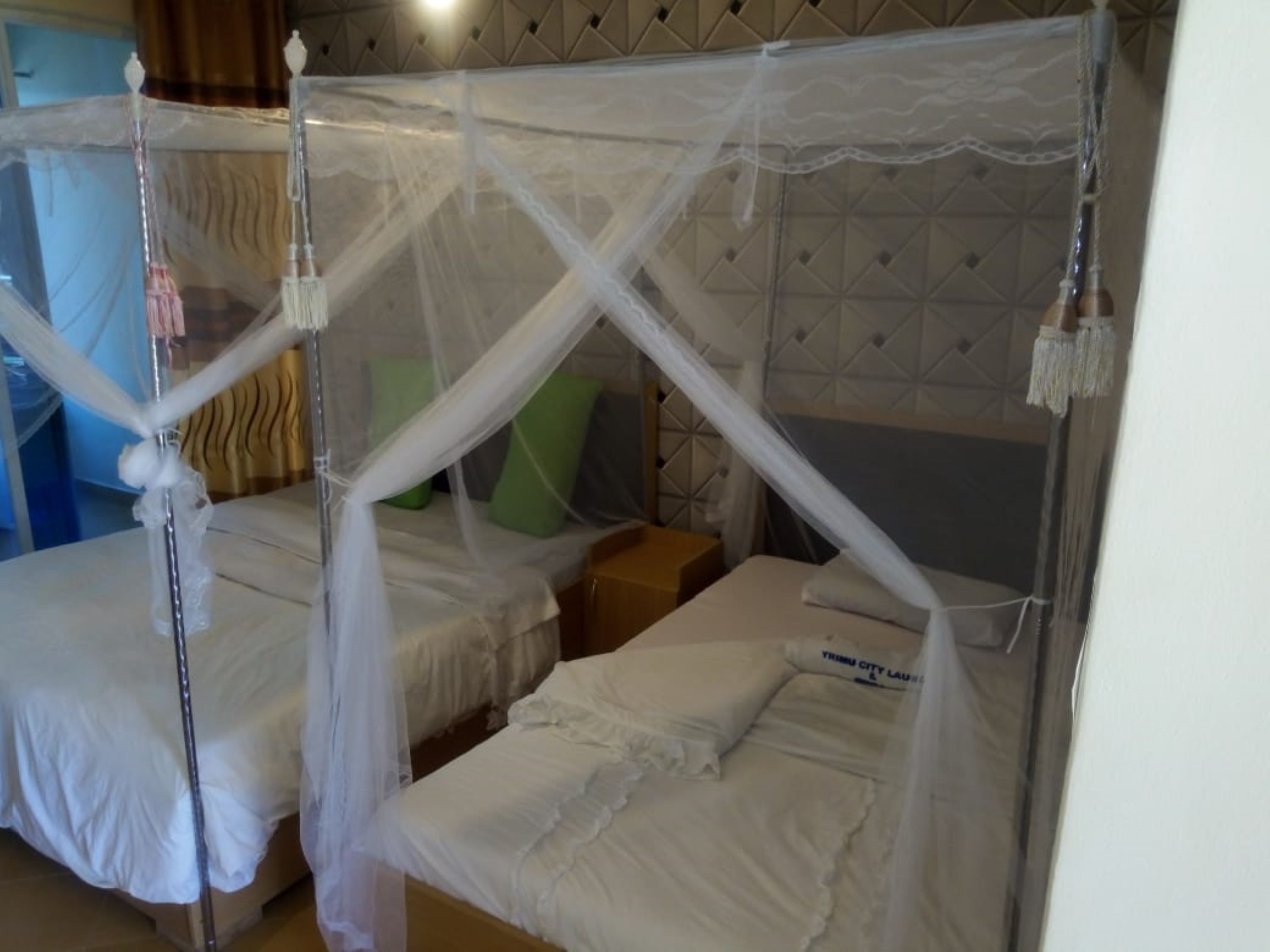 A room with two beds, each covered with white bedding and a mosquito net.