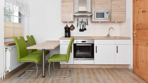 Une cuisine de taille réduite avec un plan de travail en bois, des placards blancs, un four encastré et une fenêtre équipée de stores.