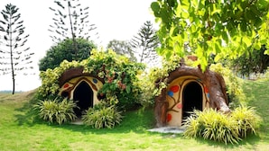 Two treehouse-like structures with arched entrances, surrounded by lush greenery and tall trees. - Vanida Resort - Halal (Ayutthaya)