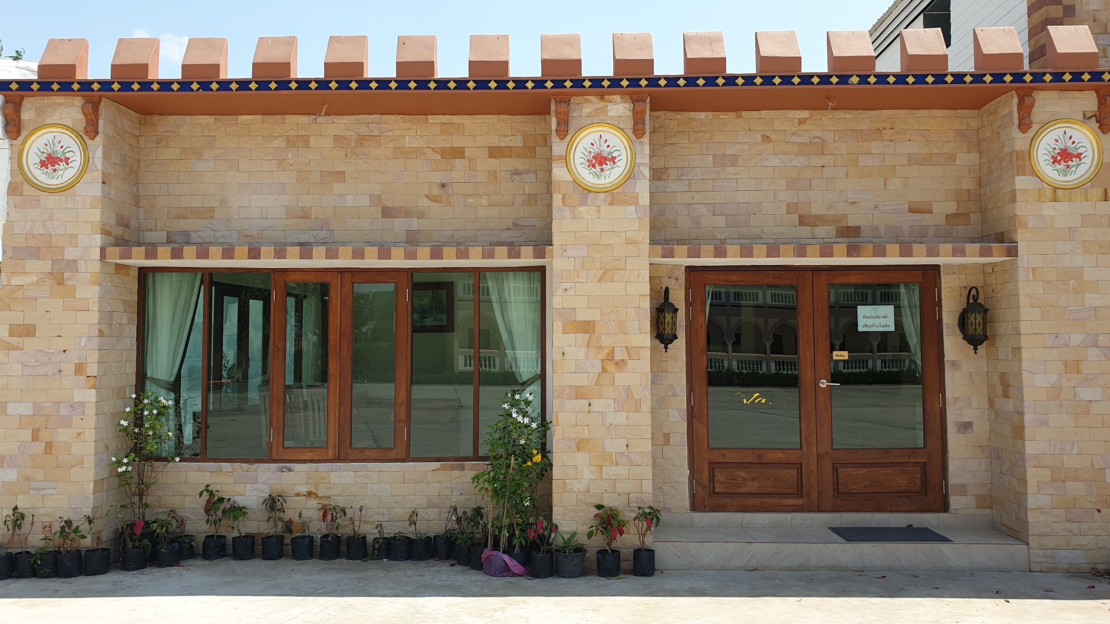 Un bâtiment avec une façade recouverte de carreaux, de grandes fenêtres et une porte en bois. Des plantes en pot sont disposées devant.