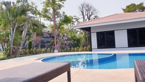 A swimming pool with lounge chairs, a modern building with large windows, and a landscaped area with rocks and trees. - Vanida Resort - Halal (Ayutthaya)