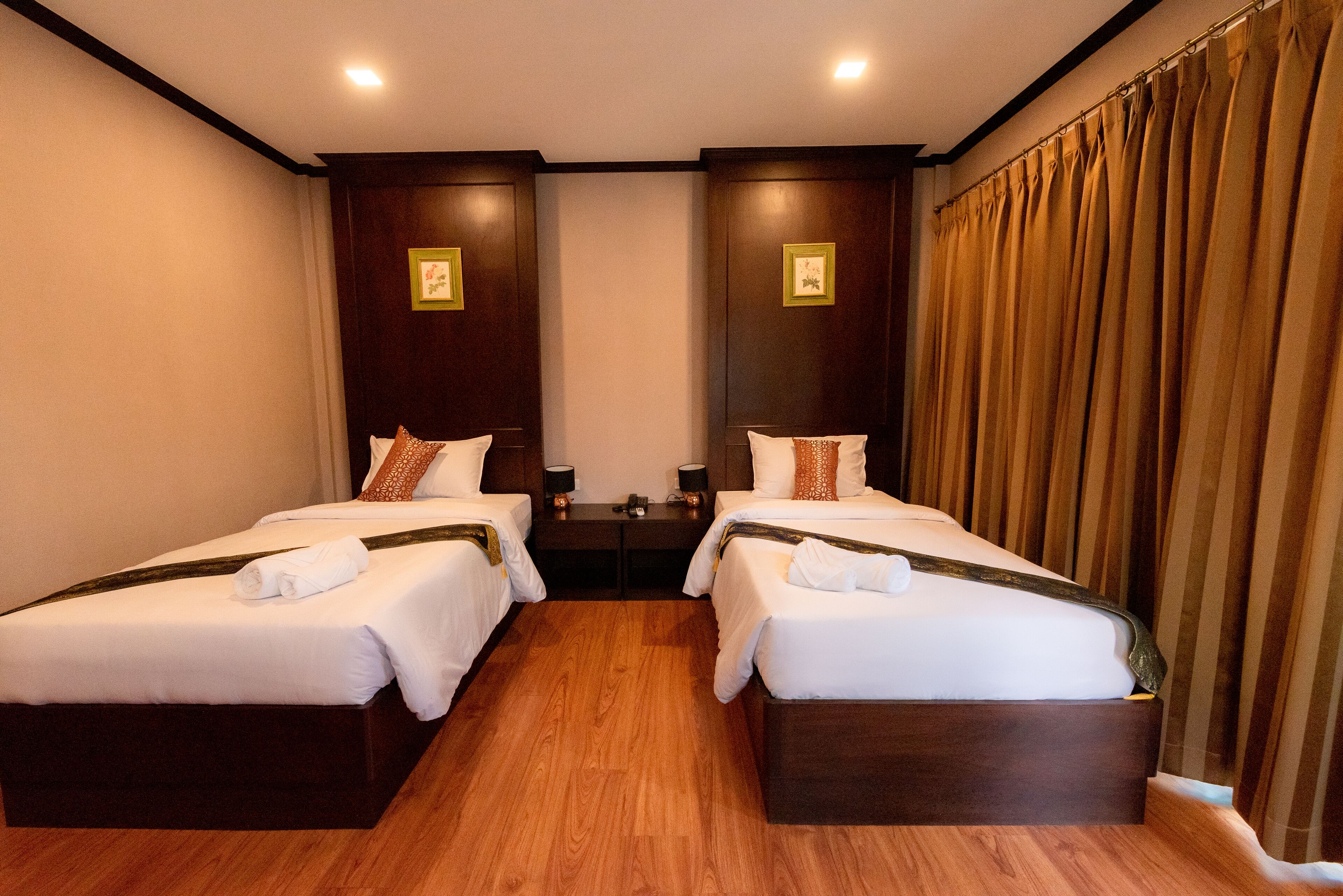 Habitación de hotel con dos camas individuales, suelo de madera, cabeceros de madera oscura y un ventanal con cortinas.