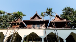 A traditional building with a tiered roof and multiple levels, surrounded by palm trees. - Vanida Resort - Halal (Ayutthaya)