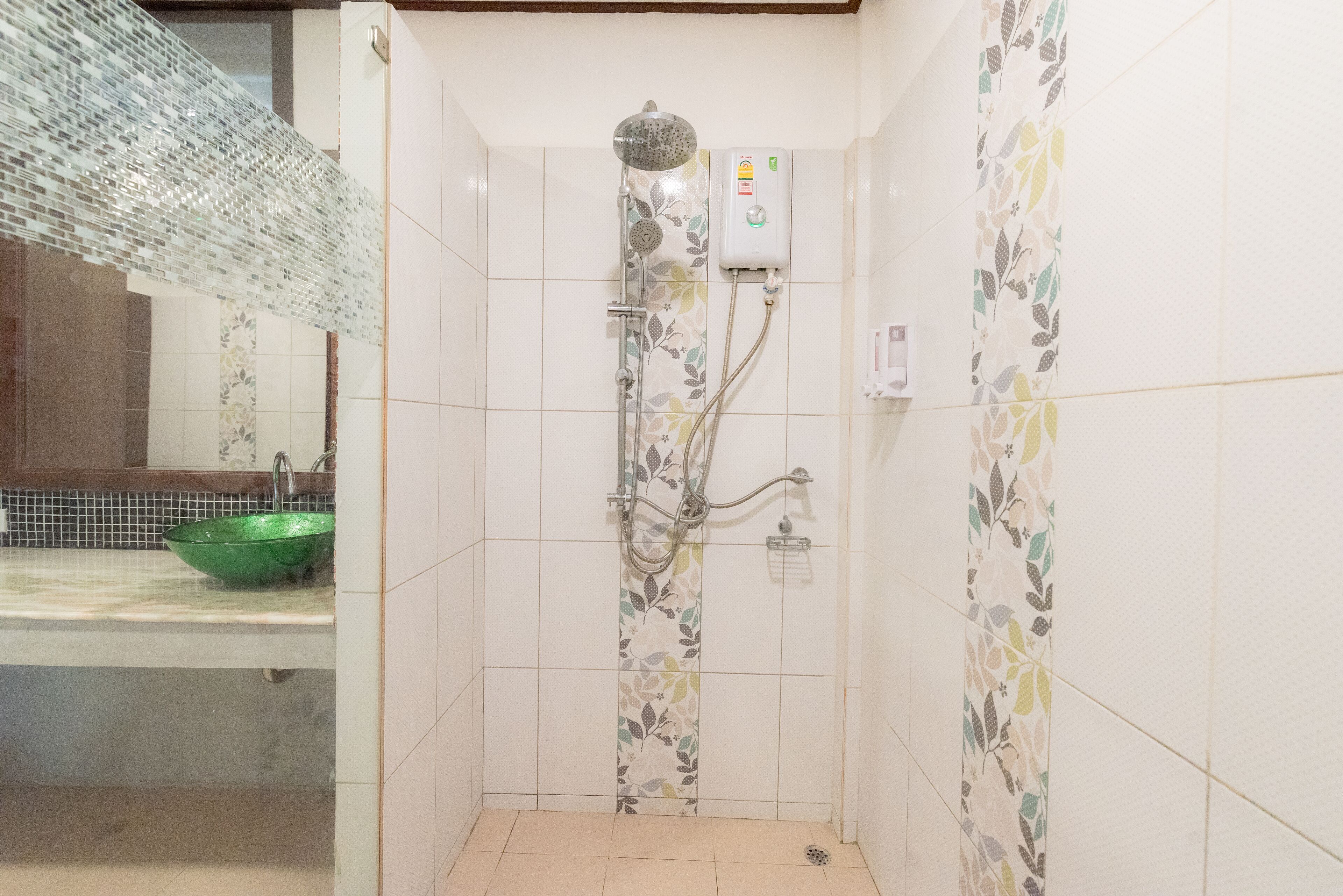 Un baño con ducha, un lavamanos verde y paredes de azulejos con estampado floral.