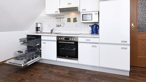 Une cuisine compacte dotée de meubles blancs, d’un lave-vaisselle, d’un four, d’un four à micro-ondes et d’une machine à café.