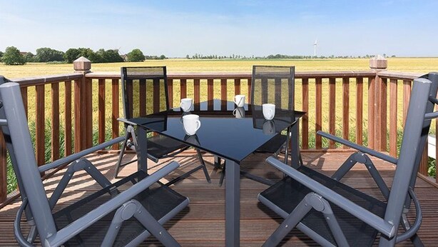 Une terrasse dotée d’une table et de chaises en verre, donnant sur un champ.